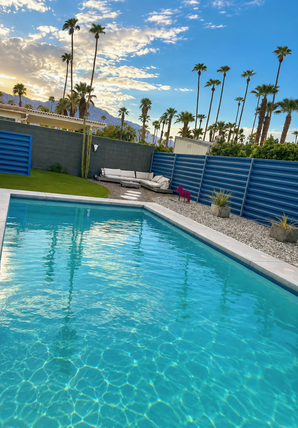 A backyard pool in the Coachella Valley, with tall palms and the mountains at sunset.